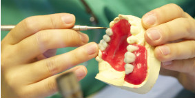 a student with an instrument in hand, manipulating wax on a plaster cast of a jaw